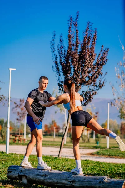 一个英俊而强壮的男人在支持他的女朋友 她单腿站在树上 两腿也正保持平衡和伸展着 — 图库照片