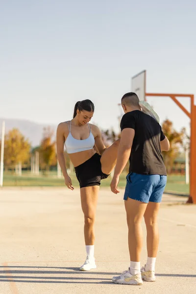 彼女の足を伸ばす彼のガールフレンドを助ける筋肉の男性スポーツ人 屋外スポーツ — ストック写真