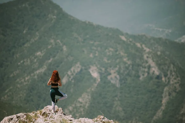 有红卷头发的瑜伽女孩在山顶做瑜伽姿势 — 图库照片