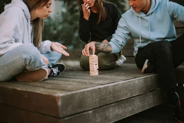 Τρεις Φίλοι Παίζουν Τζένγκα Στο Πάρκο Ενώ Κάθονται Στο Ξύλινο — Φωτογραφία Αρχείου