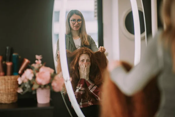 在美发店里 当一个红头发的女孩正在摸她的头发时 她在镜子前做出了令人惊讶的反应 — 图库照片