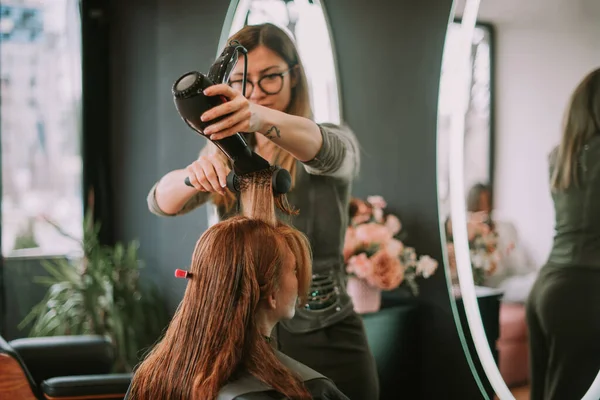 ブロンド美容師打撃乾燥彼女のクライアント毛でザヘアサロン — ストック写真