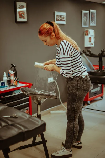 红头发的纹身艺术家正在工作室的黑色椅子上放铝箔 — 图库照片