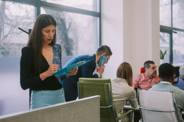 ビジネスミーティングをしている彼女の同僚の隣に立っている間にメモを書いているブルネットのビジネス女性 — ストック写真