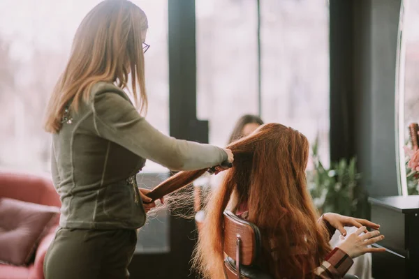 在美发师梳头的红头发姑娘坐在美发厅的椅子上的时候 — 图库照片