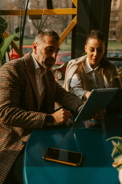 Business girl pointing on the tablet of her colleague while sitting with him at the cafe