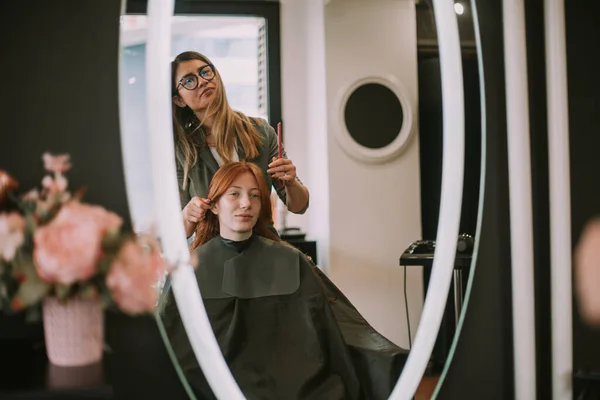 Blonde hairdresser trying some hairstyles on her ginger client while she is sitting in front of the mirror