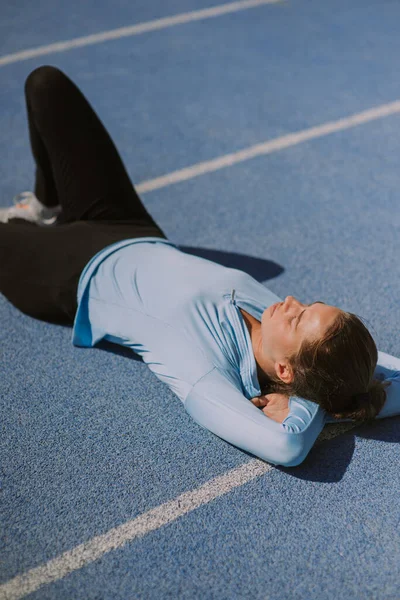Gorgeous girl is lying down on a sports track at the stadium. She is taking a brreak