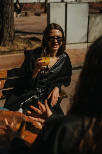 美しい晴れた日に彼女の友人とコーヒーバーに座っている間にカクテルと笑顔のガラスを保持している若い美しい女の子のショット — ストック写真