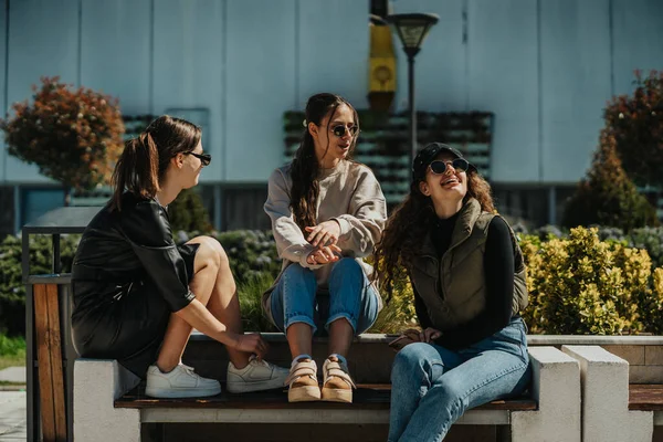 在阳光明媚的日子里 三个可爱的女孩坐在长椅上 享受着愉快的交谈 — 图库照片