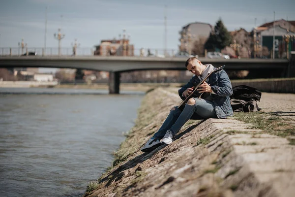 Bonito Homem Tocando Guitarra Enquanto Estava Sentado Chão Lado Rio — Fotografia de Stock