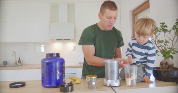 爸爸和儿子在厨房和儿子说话的时候 把坚果放进香蕉软糖里 — 图库视频影像