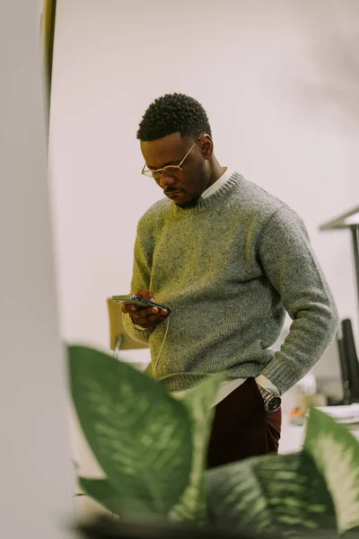若いハンサムな黒人男性がオフィスで休憩中に電話をチェックしている 彼は白い背景に立っている — ストック写真