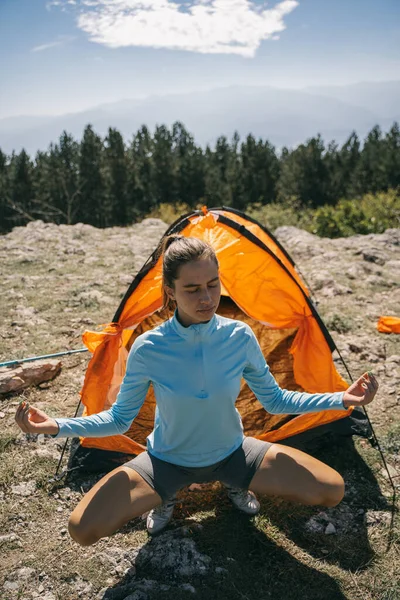 美しい少女は山の上にオレンジのテントの前で瞑想している — ストック写真