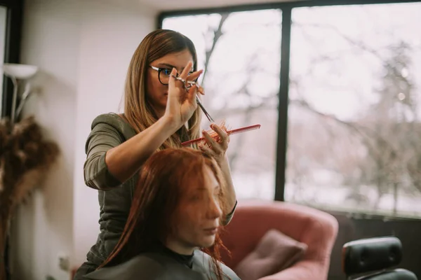 在美发厅 一个金发美发师正在给她的客户剪湿的红头发 — 图库照片