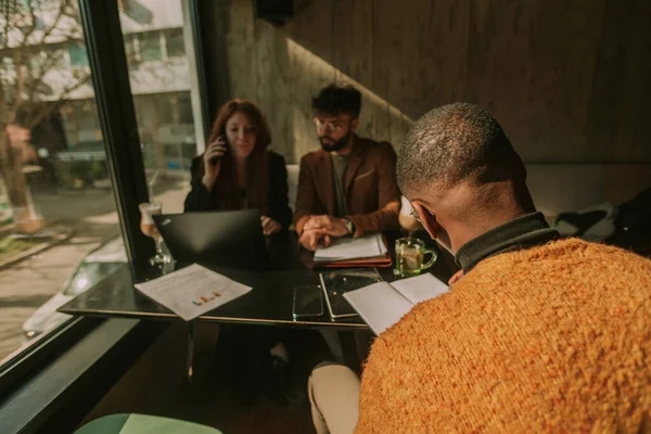 白人の同僚がテーブルの反対側の膝の上で一緒に働いている間 黒人男性ビジネス人はノートブックに新しいビジネスアイデアを書いています バックビューショット — ストック写真