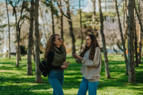 两个迷人的女孩 金发和黑发 在公园里聊天 布鲁内特姑娘向她的朋友解释一件事 — 图库照片