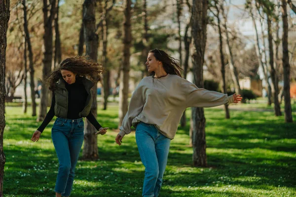 两个年轻貌美的姑娘在公园里一边听音乐一边在电话上跳舞的镜头 — 图库照片