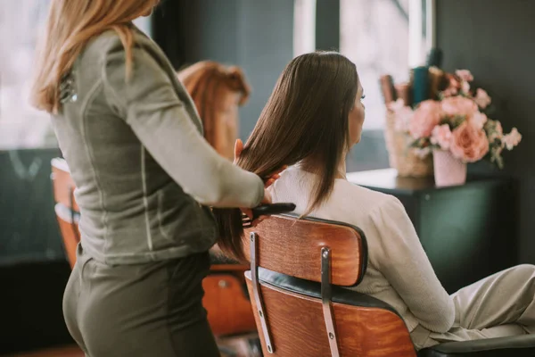Blonde hairdresser brushing her clients straight brown hair while she sits at the hair salon