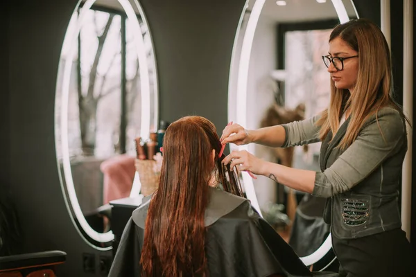 ブロンド美容師取得準備のために彼女の髪カットしながらブラッシング彼女のクライアント毛でザサロン — ストック写真