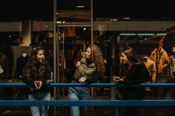 三个漂亮女孩靠在购物中心的蓝色篱笆上谈着时尚的前景照片 — 图库照片