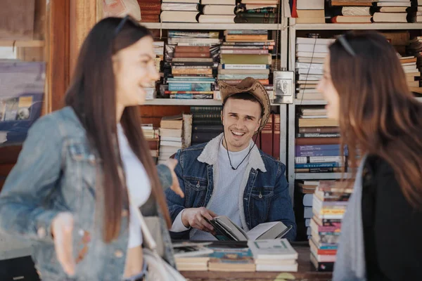 英俊的牛仔笑着看着老书店里的两个姑娘 — 图库照片