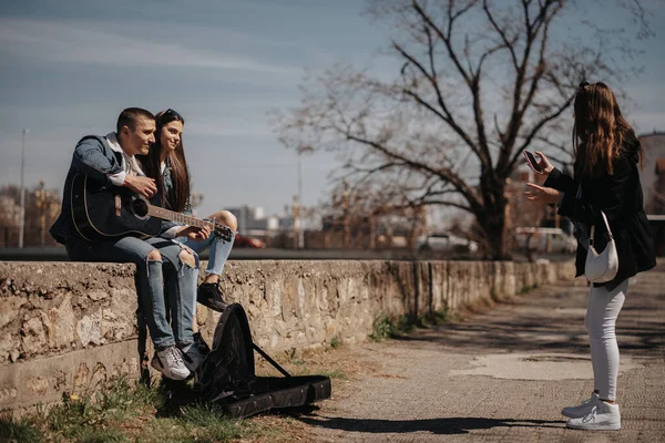 Брюнетка Пытается Сфотографировать Красивую Пару Сидящую Парке Гитарой — стоковое фото