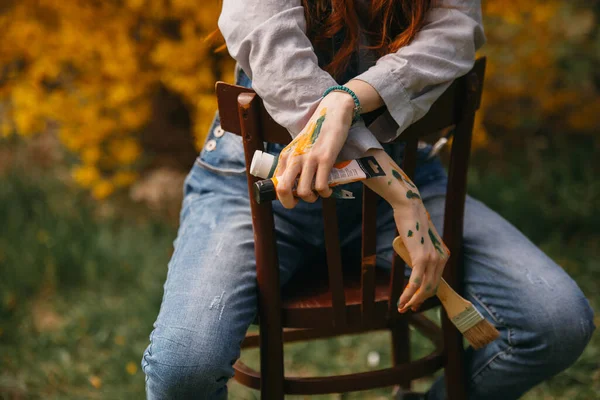 公園で木製の椅子に座っている間にペイントチューブを保持している画家の女の子の閉鎖 — ストック写真