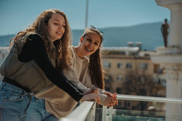 美しい若い女の子が建物の上のフェンスにもたれて 通りに何か面白いものを見た 笑ってる — ストック写真