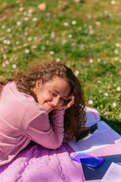 卷发女孩躺在公园里的紫色毯子上 和她的朋友聊着天 面带微笑 — 图库照片