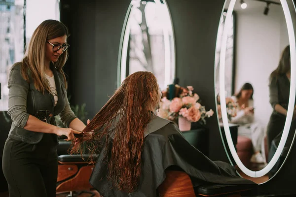 金发美发师在美发厅给客人刷红头发和湿头发 — 图库照片