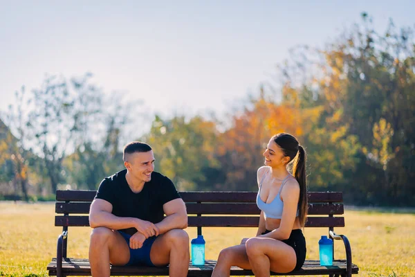 美しいカップルが公園で遊んでいます 彼らはベンチに座って面白い会話をしています — ストック写真