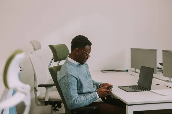 Młody Afrykański Biznesmen Patrzy Telefon Siedząc Przy Biurku Miejscu Pracy — Zdjęcie stockowe