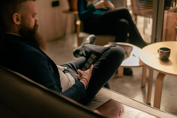 Sakallı Adam Kafede Bacak Bacak Üstüne Atmış Telefonuyla Kayıyor — Stok fotoğraf