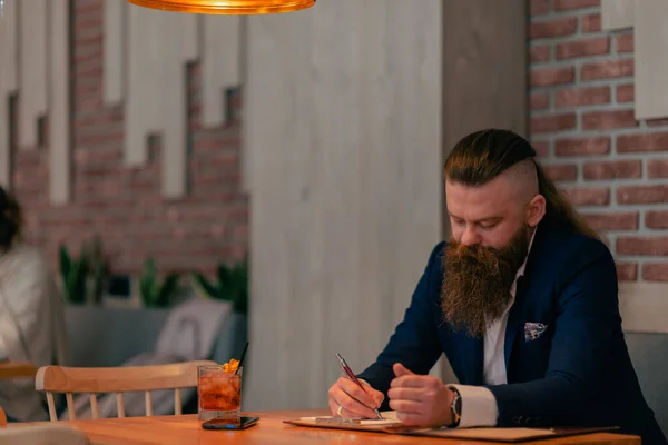 カフェでペンでノートに何か書いてる髭の男 — ストック写真