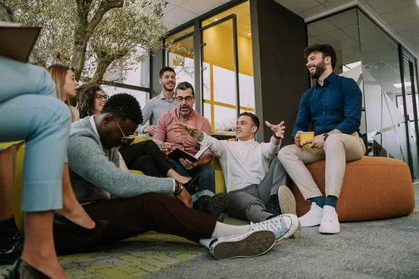 複数の人種の同僚のグループは 彼らに面白いことを説明する若い同僚に耳を傾けます 笑ってる — ストック写真