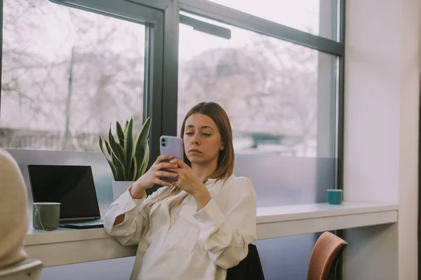 Κουρασμένη Ξανθιά Επιχειρηματίας Ελέγχει Τηλέφωνό Της Ενώ Κάθεται Ένα Γραφείο — Φωτογραφία Αρχείου
