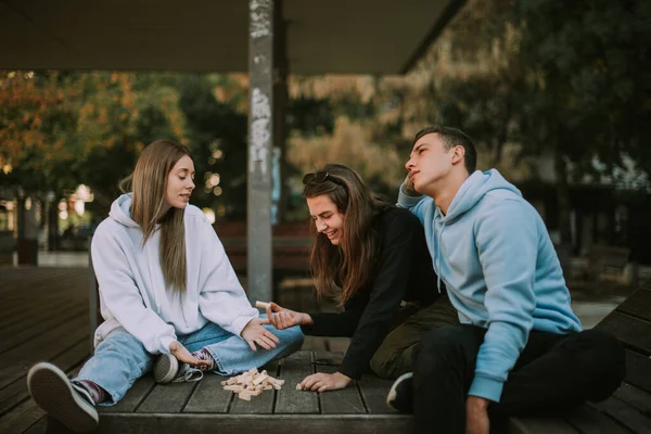 Drei Freunde Sitzen Auf Der Holzbank Mit Verstreutem Jenga — Stockfoto