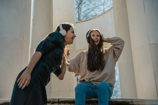 stock image Two beautiful girls listening to music on their headphones and laughing. Enjoying the summer day in the park