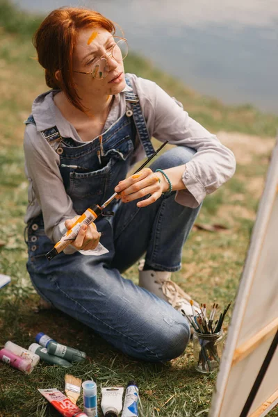 Zblízka Krásné Zázvor Dívka Malování Plátno Barvou Tváři Sedí Trávě — Stock fotografie