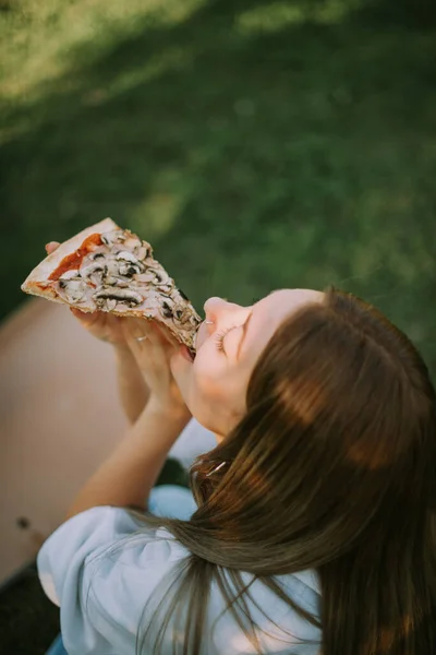 Όμορφη Κοπέλα Τρώει Πίτσα Ενώ Κάθεται Στο Πάρκο Στο Γρασίδι — Φωτογραφία Αρχείου