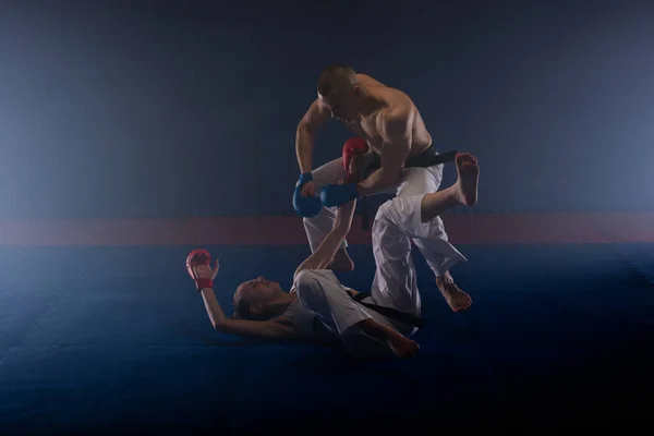 空手スタジオの床で戦っている2人の若者と強い空手の人々 — ストック写真