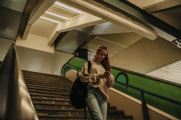 女の子は地下鉄で階下に歩いて彼女の電話を見た 彼女はバッグを持っている — ストック写真
