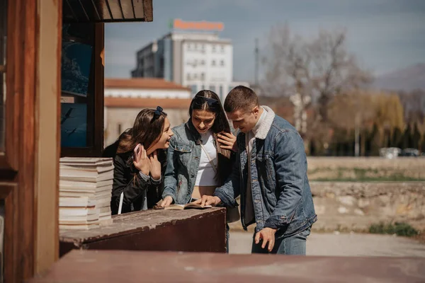 Τρεις Φίλοι Κοιτάζουν Βιβλίο Και Μιλάνε Και Χαμογελούν Ενώ Στέκονται — Φωτογραφία Αρχείου