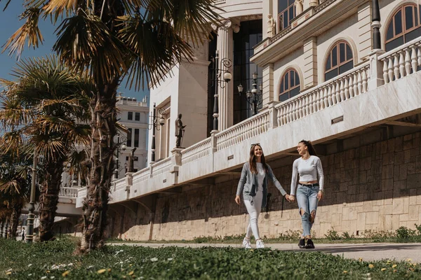 Duas Garotas Bonitas Andando Parque Frente Aos Edifícios Mãos Dadas — Fotografia de Stock