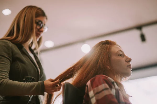一位金发美发师站在美发厅前给客人编了个红头发的辫子 — 图库照片