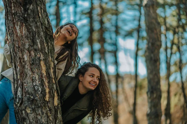 两个漂亮的女孩在看到有趣的事之后笑了 他们躲在公园的树后 — 图库照片