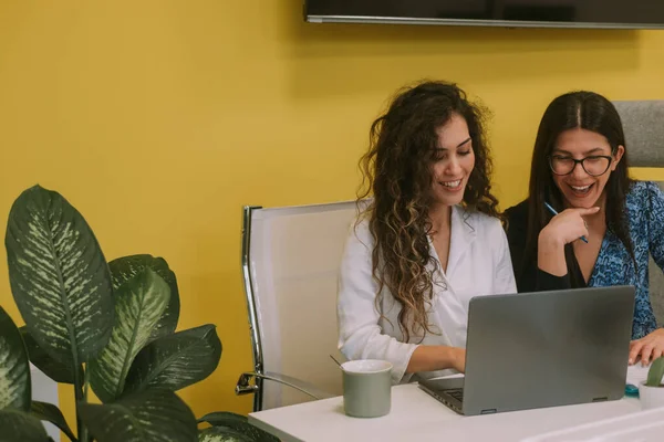 两个漂亮的女商人坐在共同工作的空间里 一边笑着笔记本电脑里的什么东西 — 图库照片
