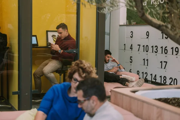 商人们一边坐在共同工作的空间里一边看着他们的手机 — 图库照片