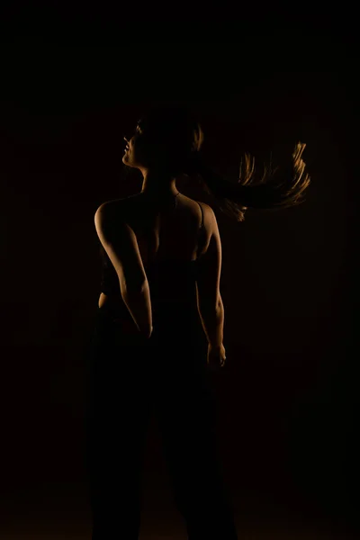 スタジオでポーズを取りながらセクシーな女の子が髪を飛んでいます 彼女は黒い服を着ている バックビュー — ストック写真